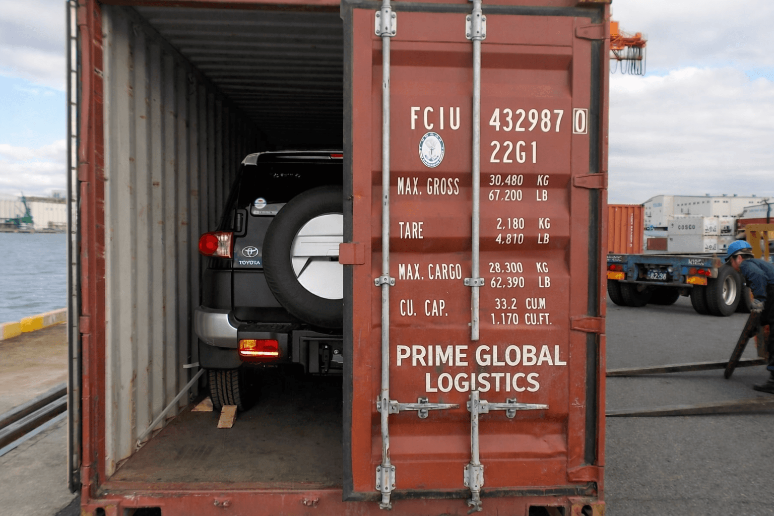 Black Toyota FJ Cruiser secured inside an open shipping container at a port with Prime Global Logistics markings on the door